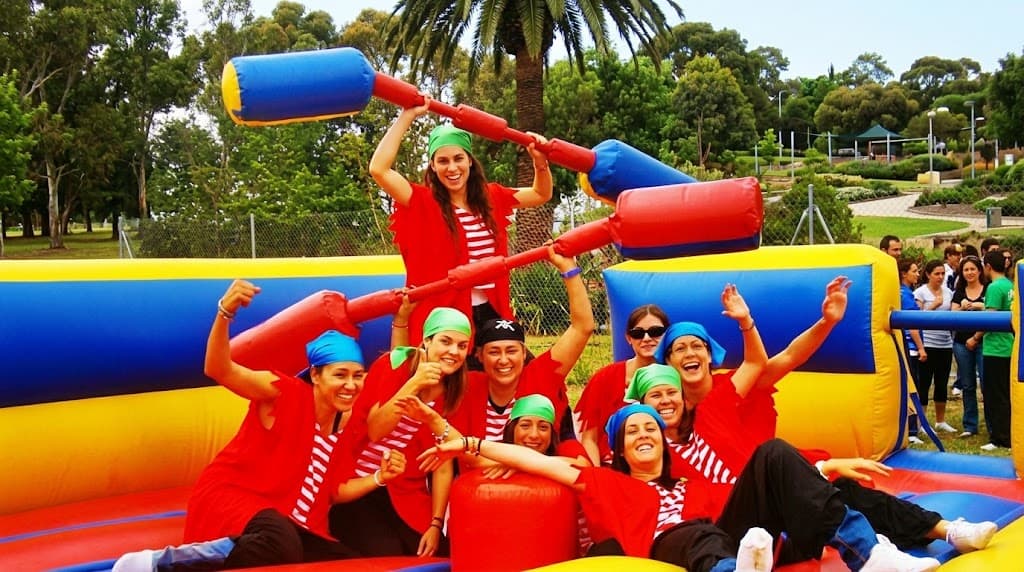 Mujeres disfrazadas de piratas posan en una arena inflable con bastones de gladiador gigantes.