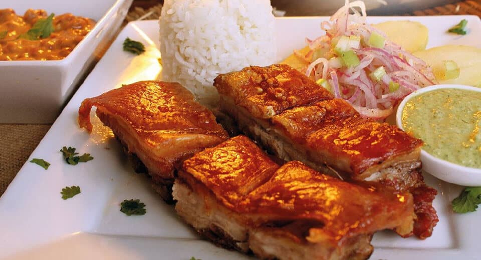 Chicharrón de cerdo crujiente servido con arroz blanco, ensalada de cebolla y salsa verde.