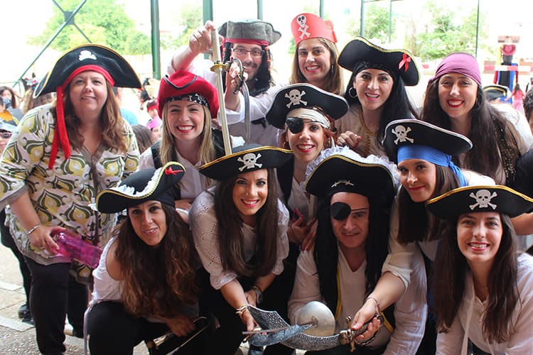 Grupo de personas sonrientes disfrazadas de piratas con sombreros, parches y espadas de juguete.