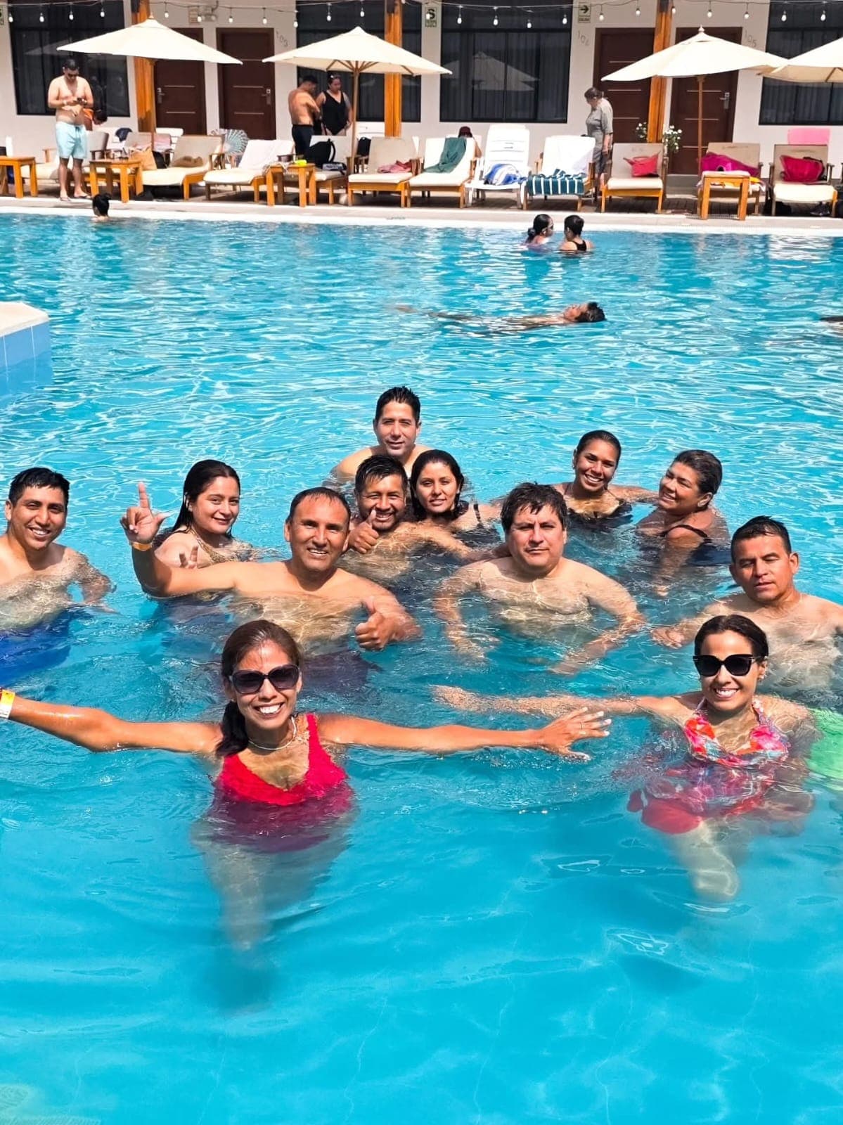 Grupo de personas sonrientes posando juntas en una piscina azul bajo el sol brillante.