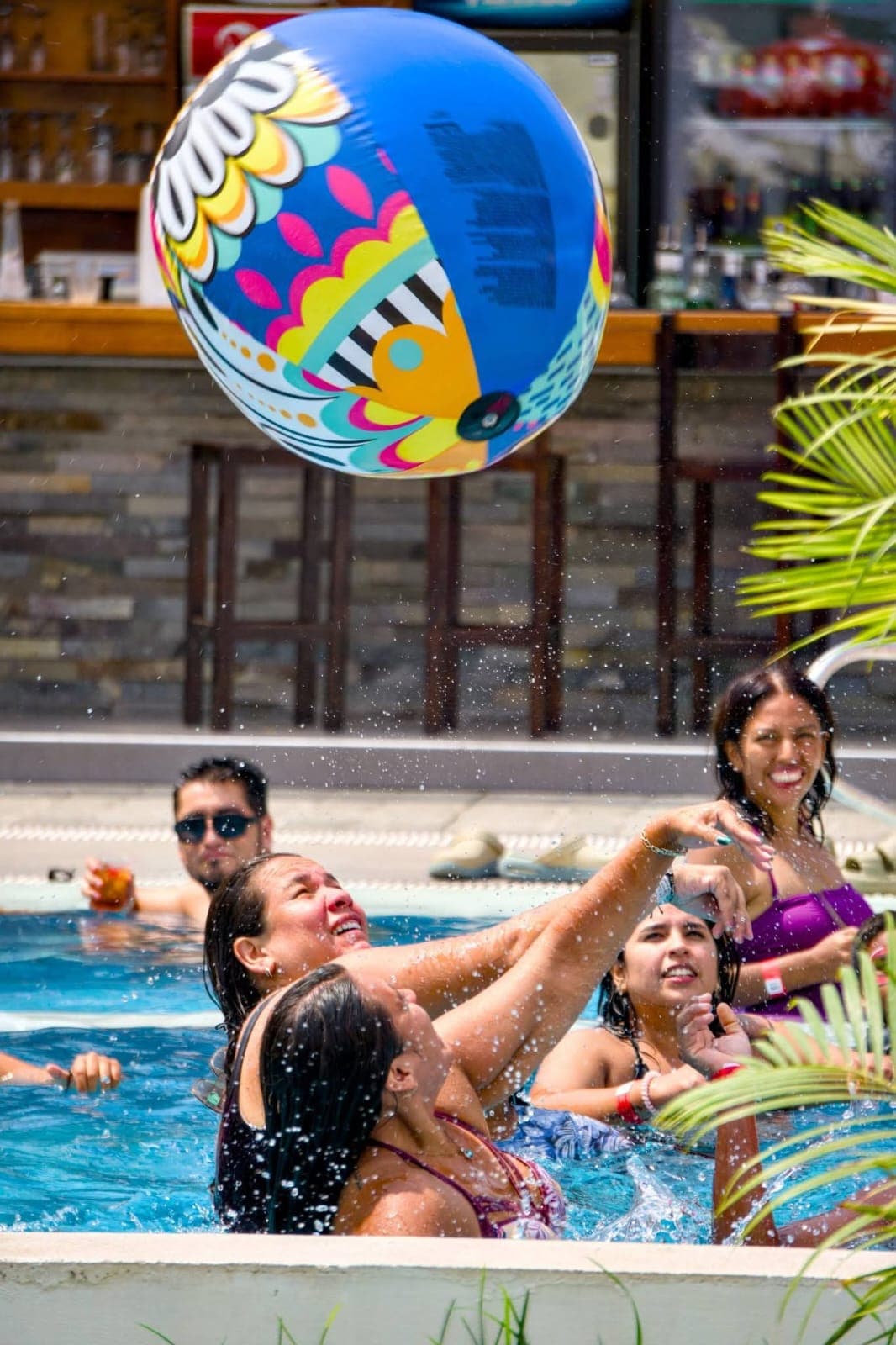 Gente en una piscina intentando atrapar una gran pelota de playa colorida entre salpicaduras.