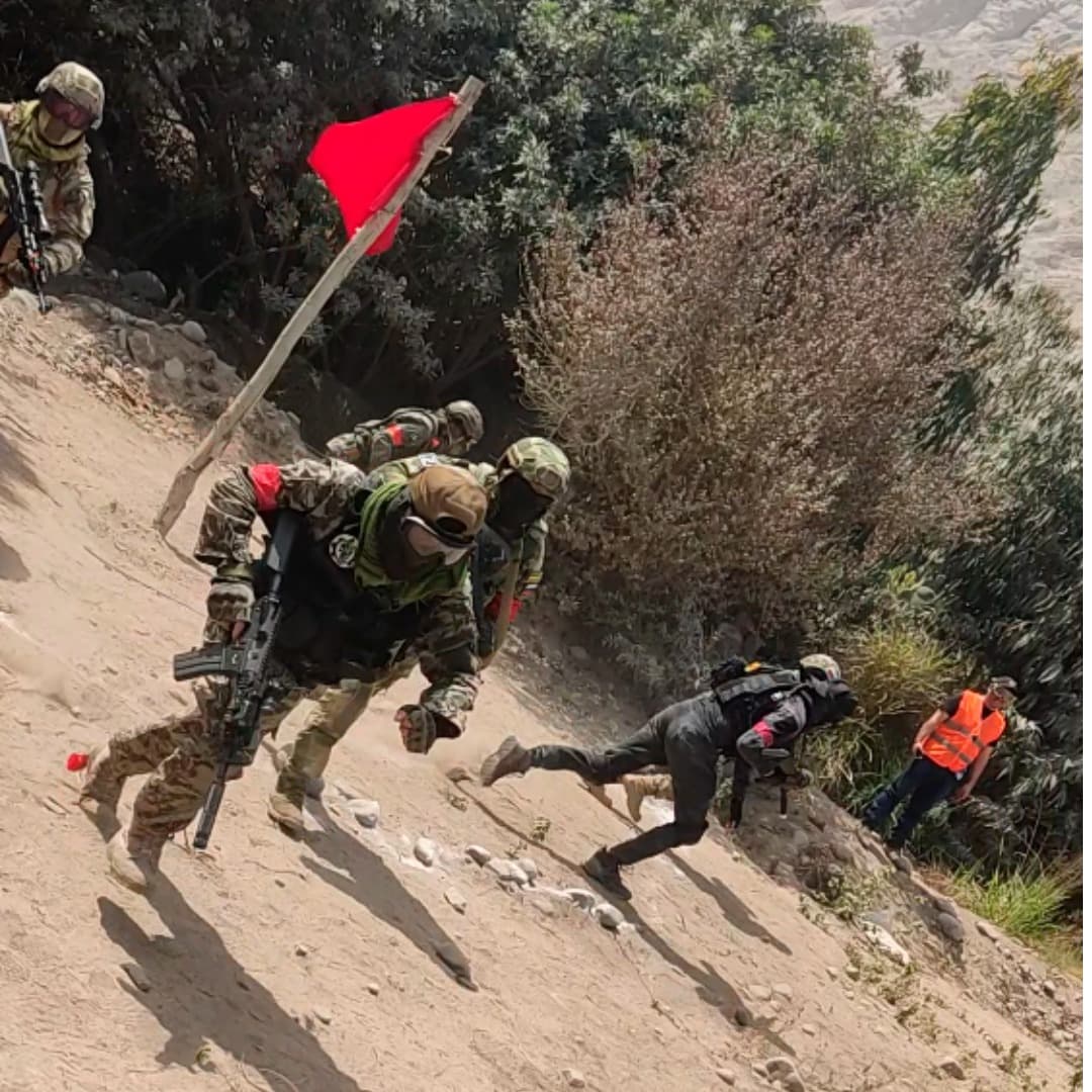 Jugadores tácticos con camuflaje suben corriendo una colina empinada junto a una bandera roja.