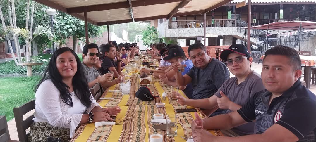 Grupo de personas sentadas en una mesa larga con manteles amarillos en un restaurante exterior.